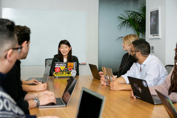 Board room photo, staff fit at a brown table with laptops looking at someone speaking