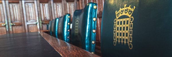 An image of House of Commons green parliamentary chairs against a brown table.