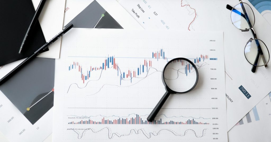 An image of a fluctuating graph on a sheet of paper with a magnifying glass lying on top.